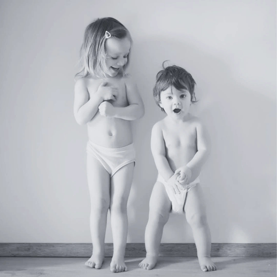 Deux enfants souriants portant des culottes d’apprentissage, prêts pour la transition vers la propreté. Une image de complicité et de réussite.